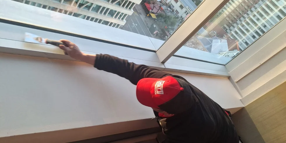 Técnico de MET ONE sellando el marco de un ventanal en un piso alto de un hotel